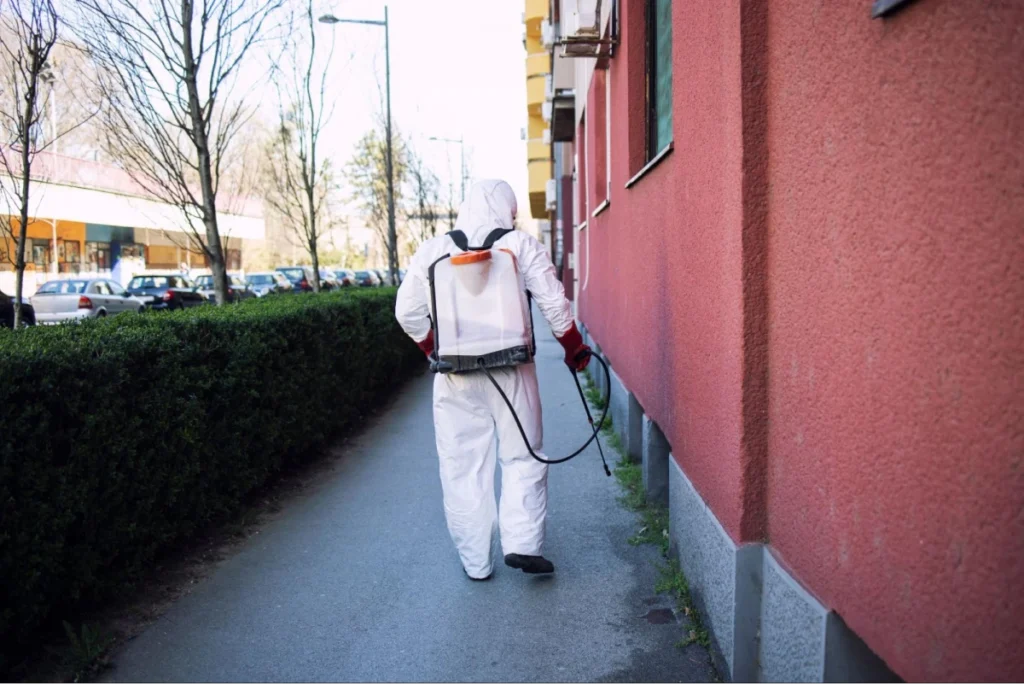 Worker in hazmat suit spraying sidewalk.