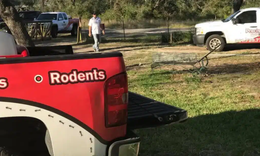 A pest control truck labeled with "Rodents" and "Precision Pest Control" parked on a grassy area near a rural property.