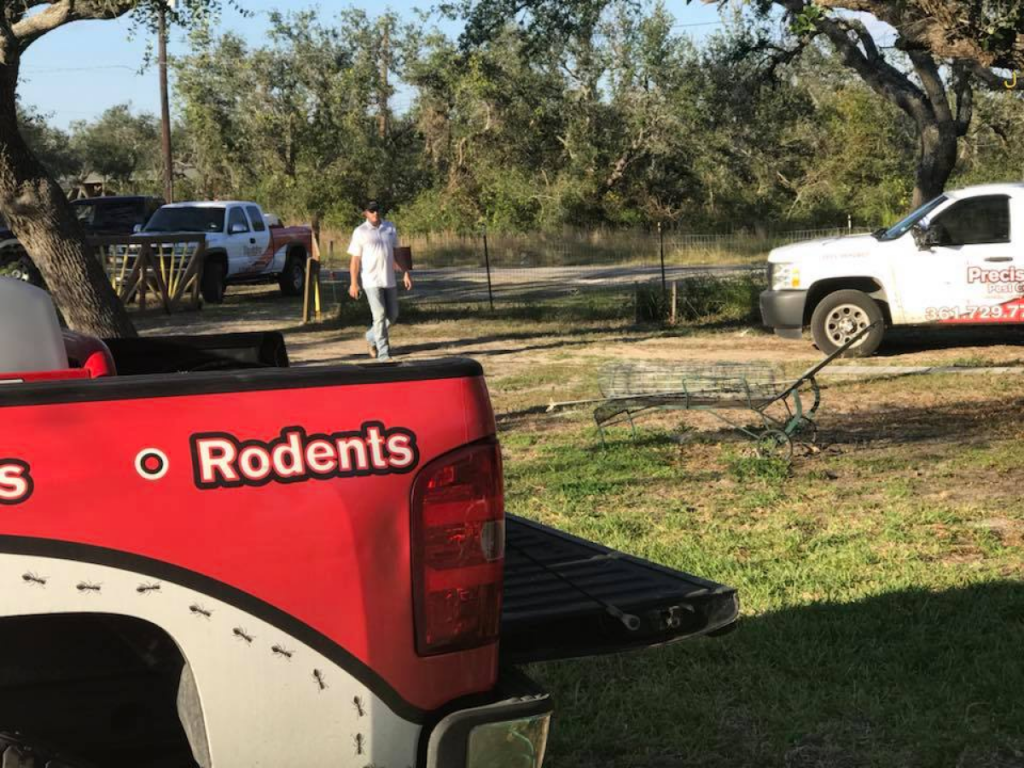 A pest control truck labeled with "Rodents" and "Precision Pest Control" parked on a grassy area near a rural property.