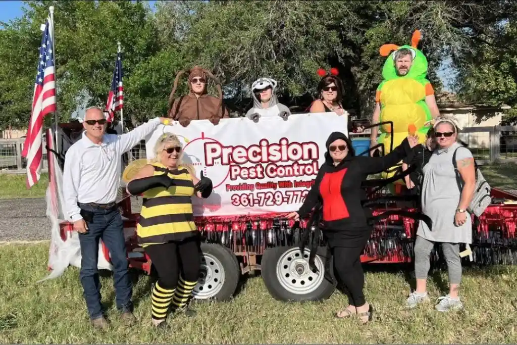 People in insect costumes posing by a Precision Pest Control banner on a decorated float