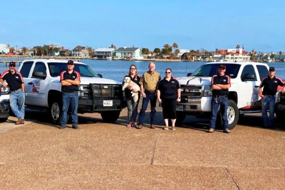 Team posing with branded trucks near a waterfront with houses in the background
